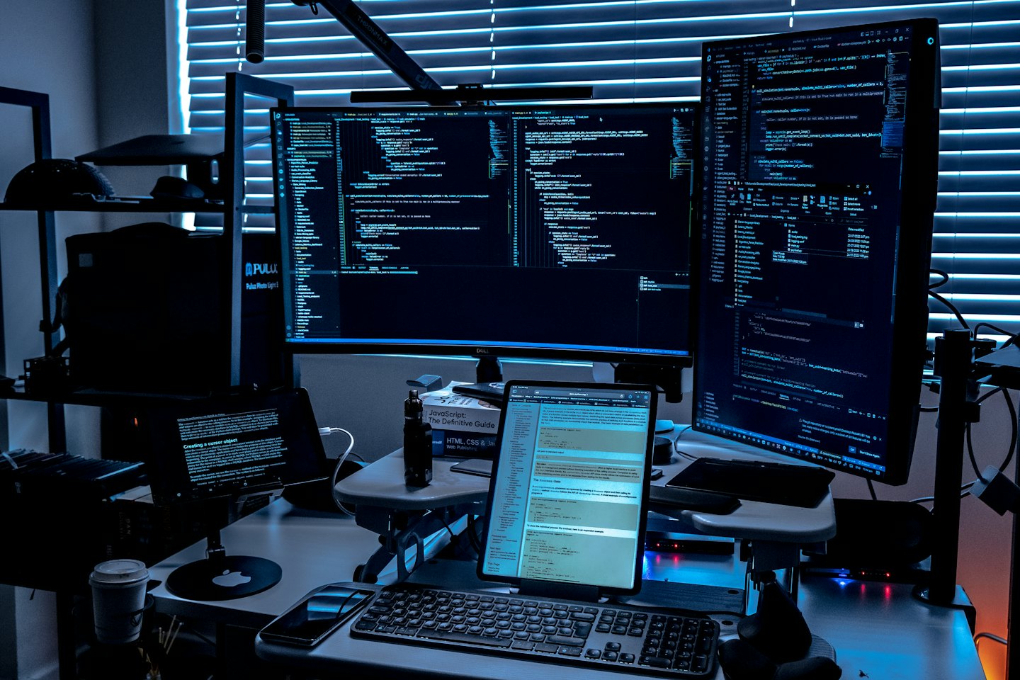 Due grandi monitor e un portatile con codice in un ufficio buio.